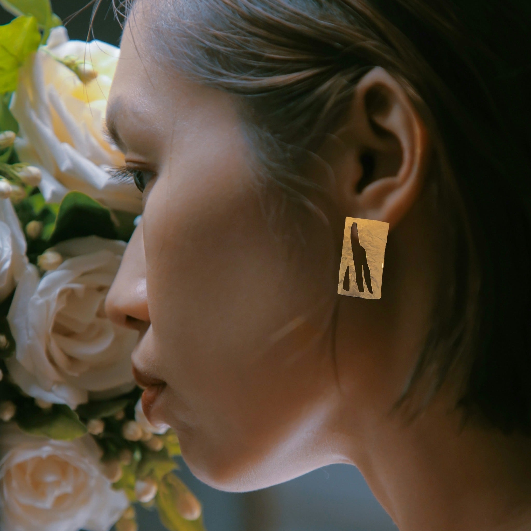 Close-up of a person wearing a gold earring with a hand design, surrounded by flowers.