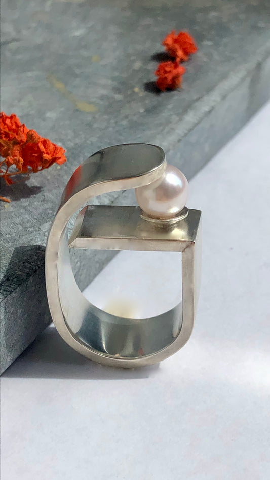 Silver ring with a pearl on a gray surface with flowers in the background