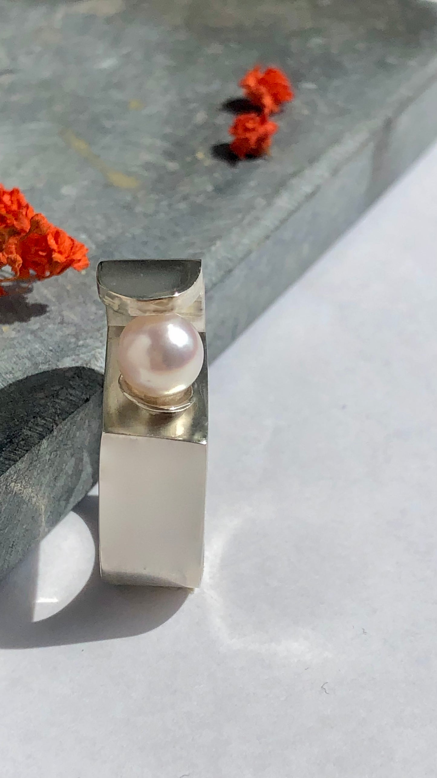 Silver ring with a pearl on a light surface with orange flowers in the background