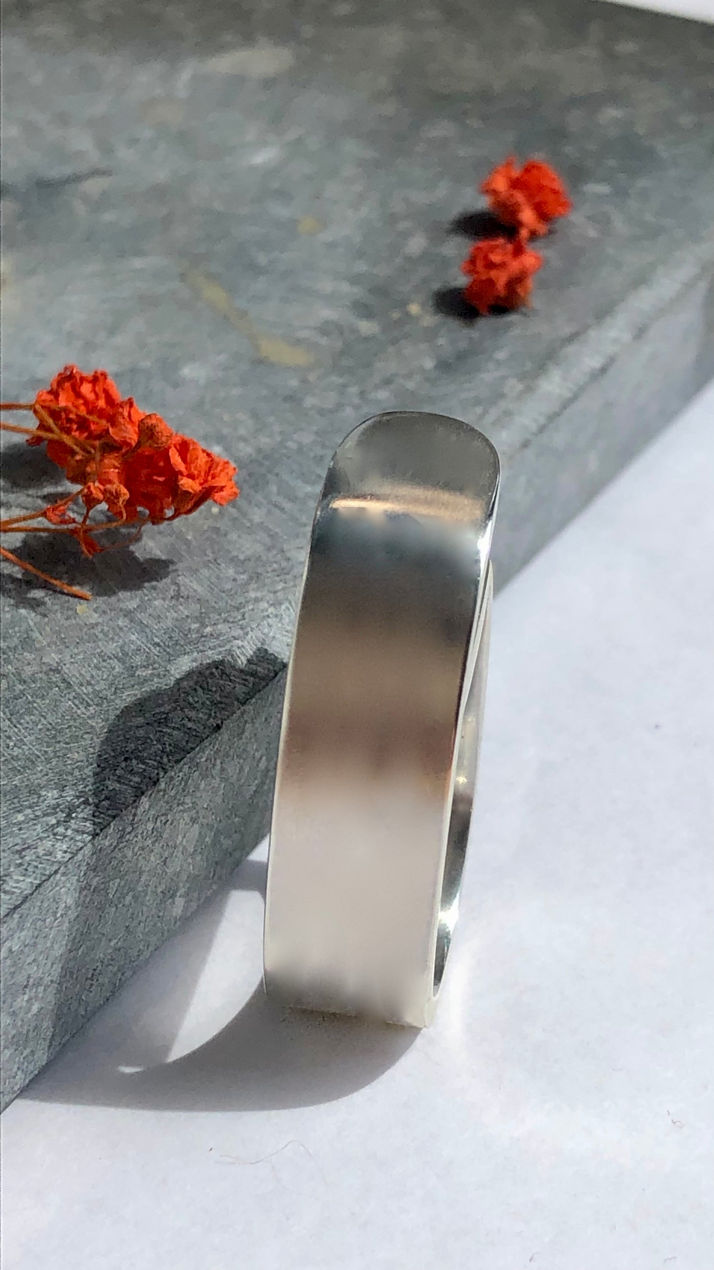 Silver chunky ring on a stone surface with dried orange flowers.