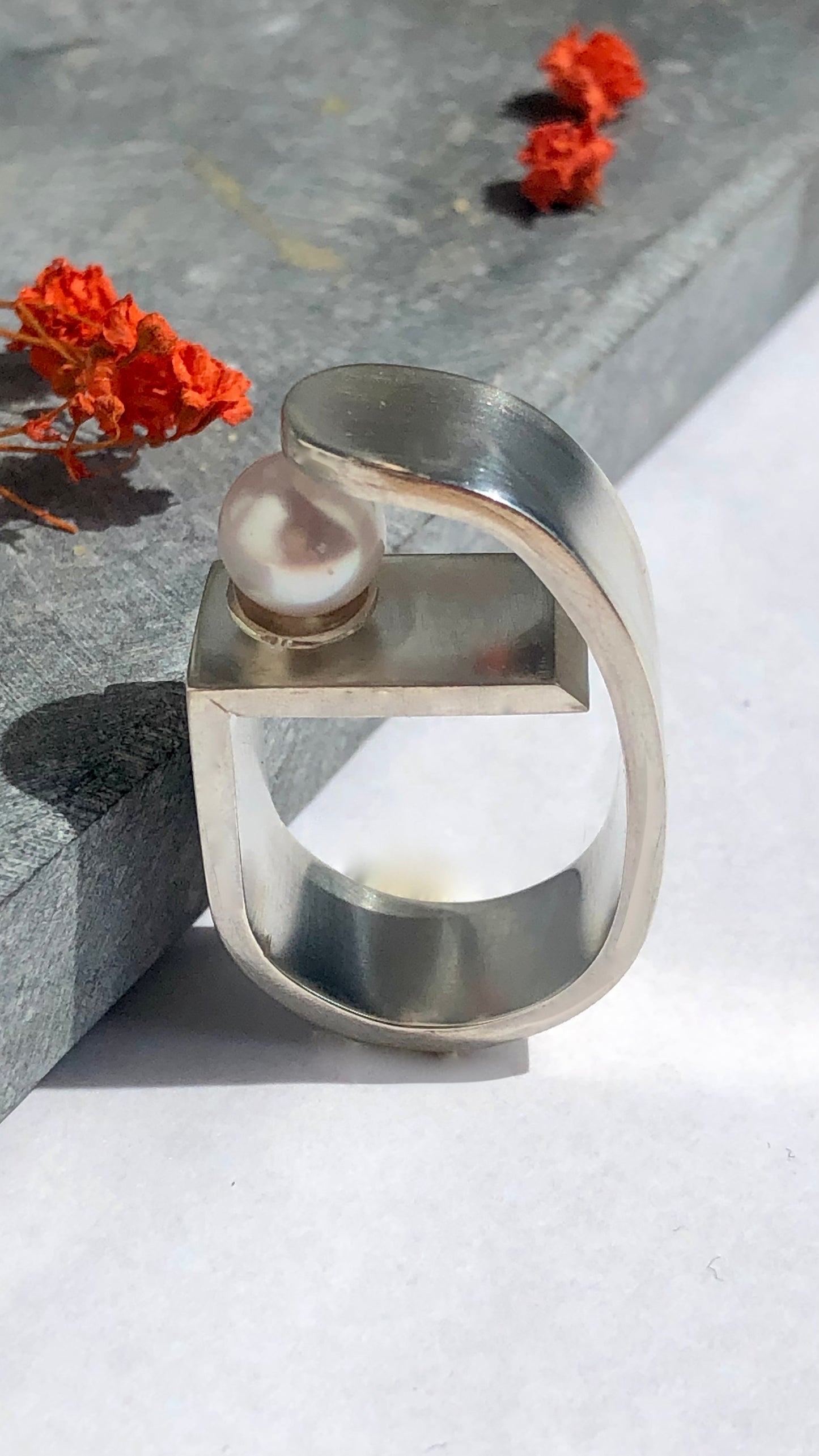 Silver ring with a pearl on a gray surface with orange flowers.