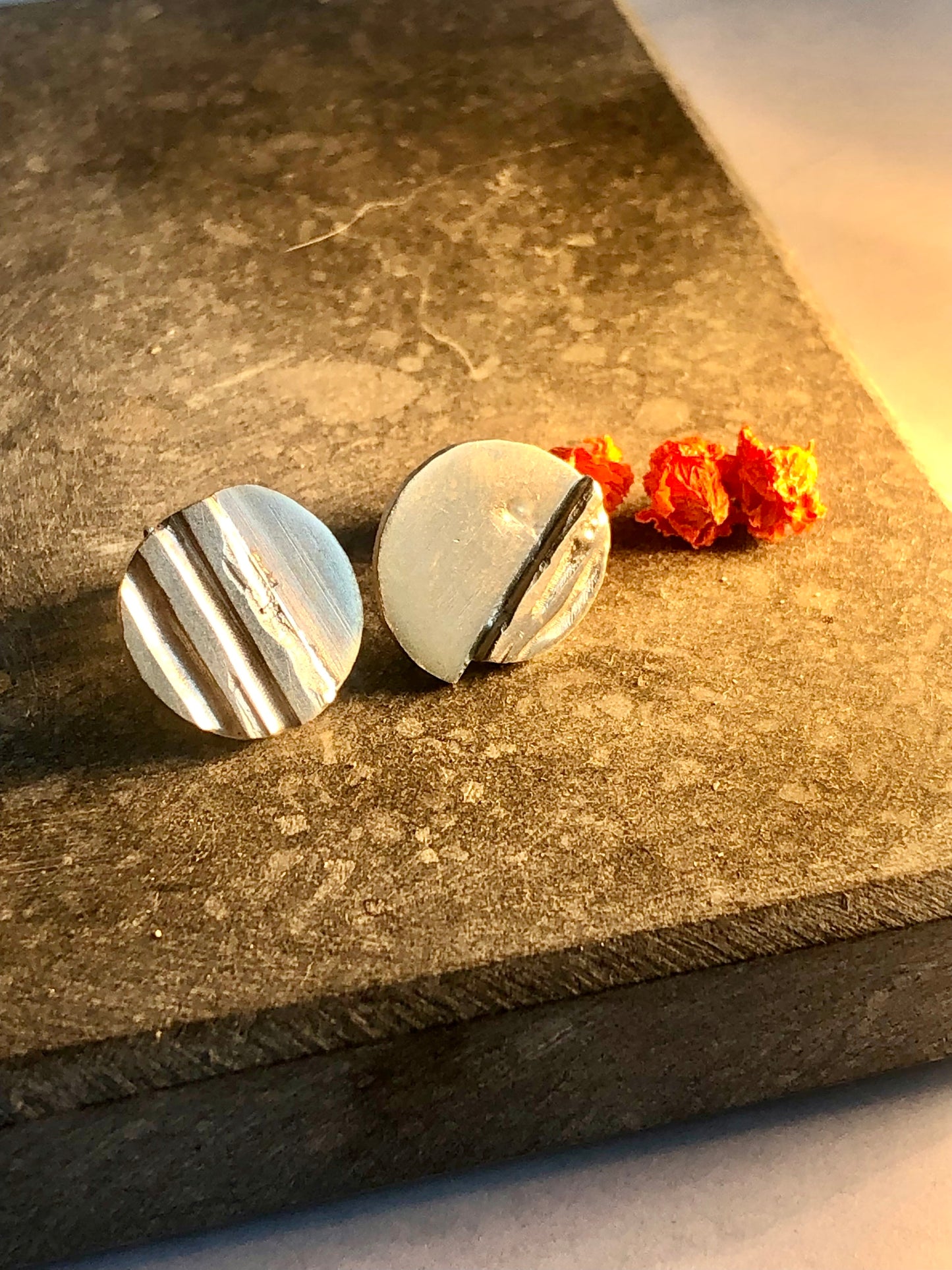 Round silver earrings on a textured stone surface with orange flowers.