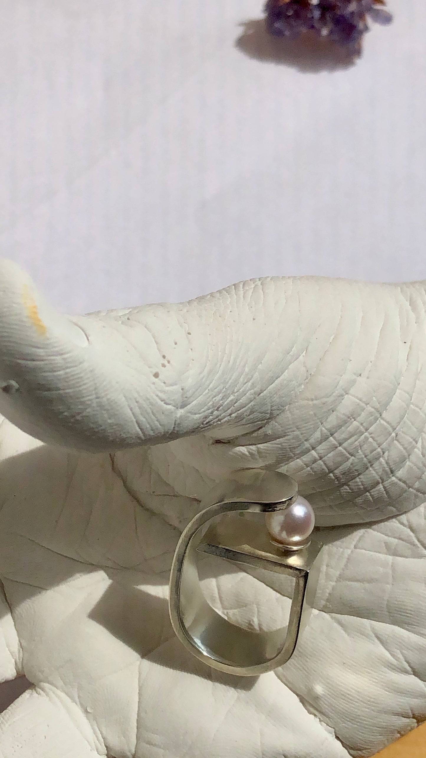 Close-up of a pearl ring on a white hand figurine with a light purple background.