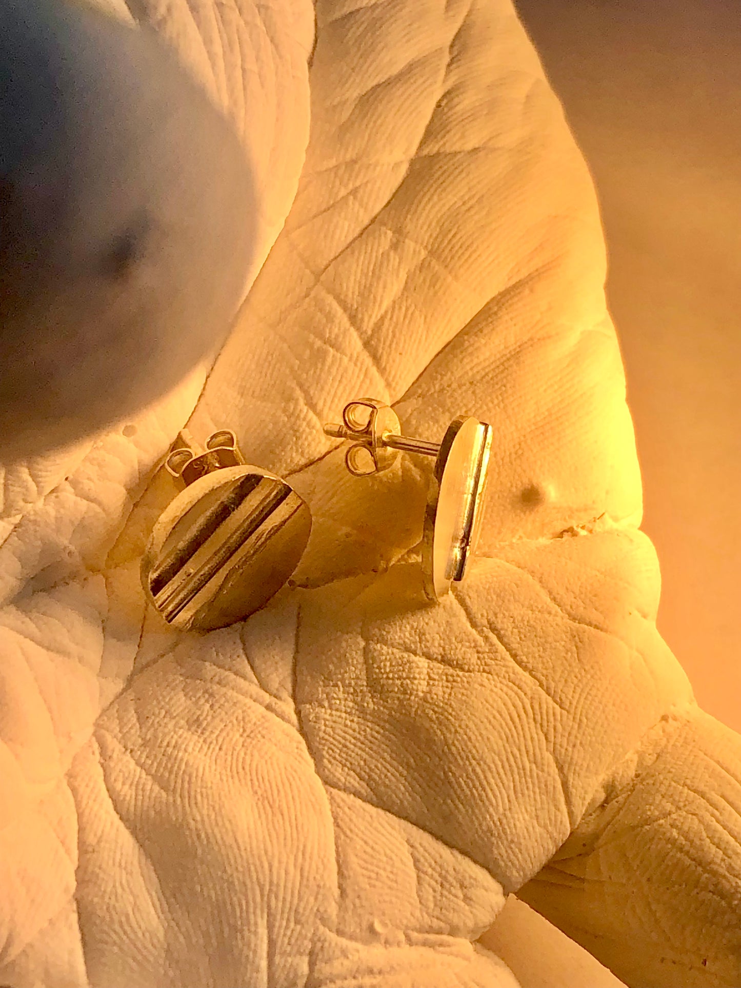 silver earrings on a textured surface of hand sculpture in golden glow