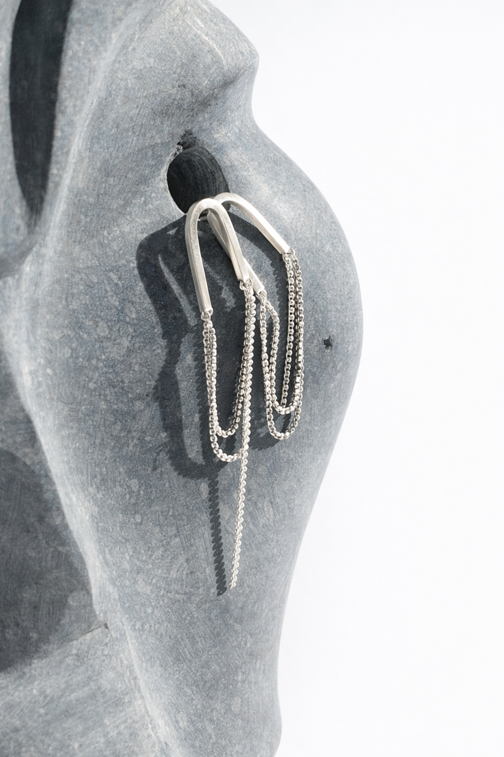 Silver earring on a mannequin ear with a plain background