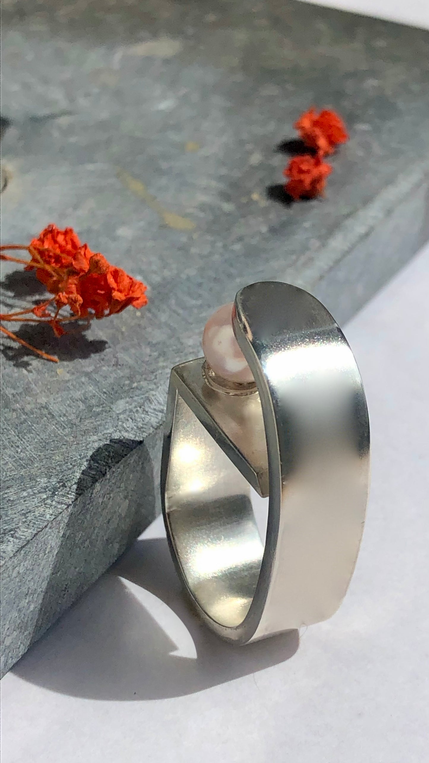Silver ring with a pearl on a stone surface with orange flowers