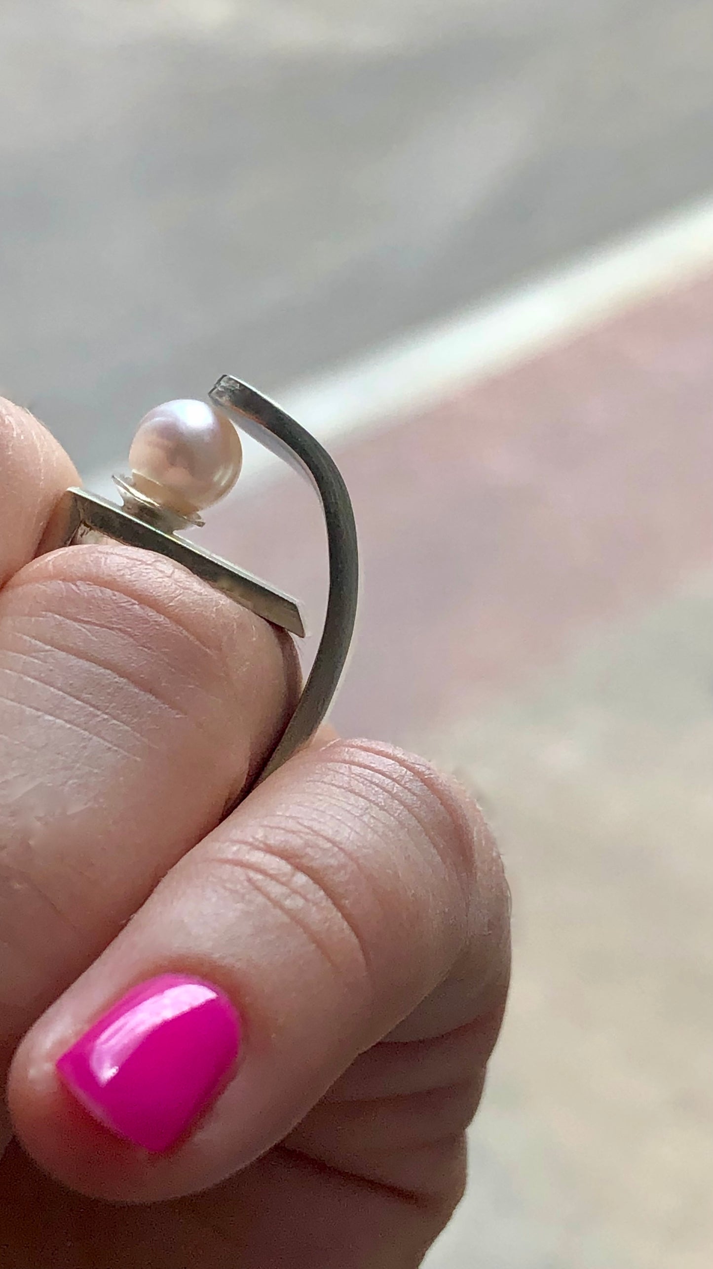 Hand wearing a ring with a pearl on a blurred background