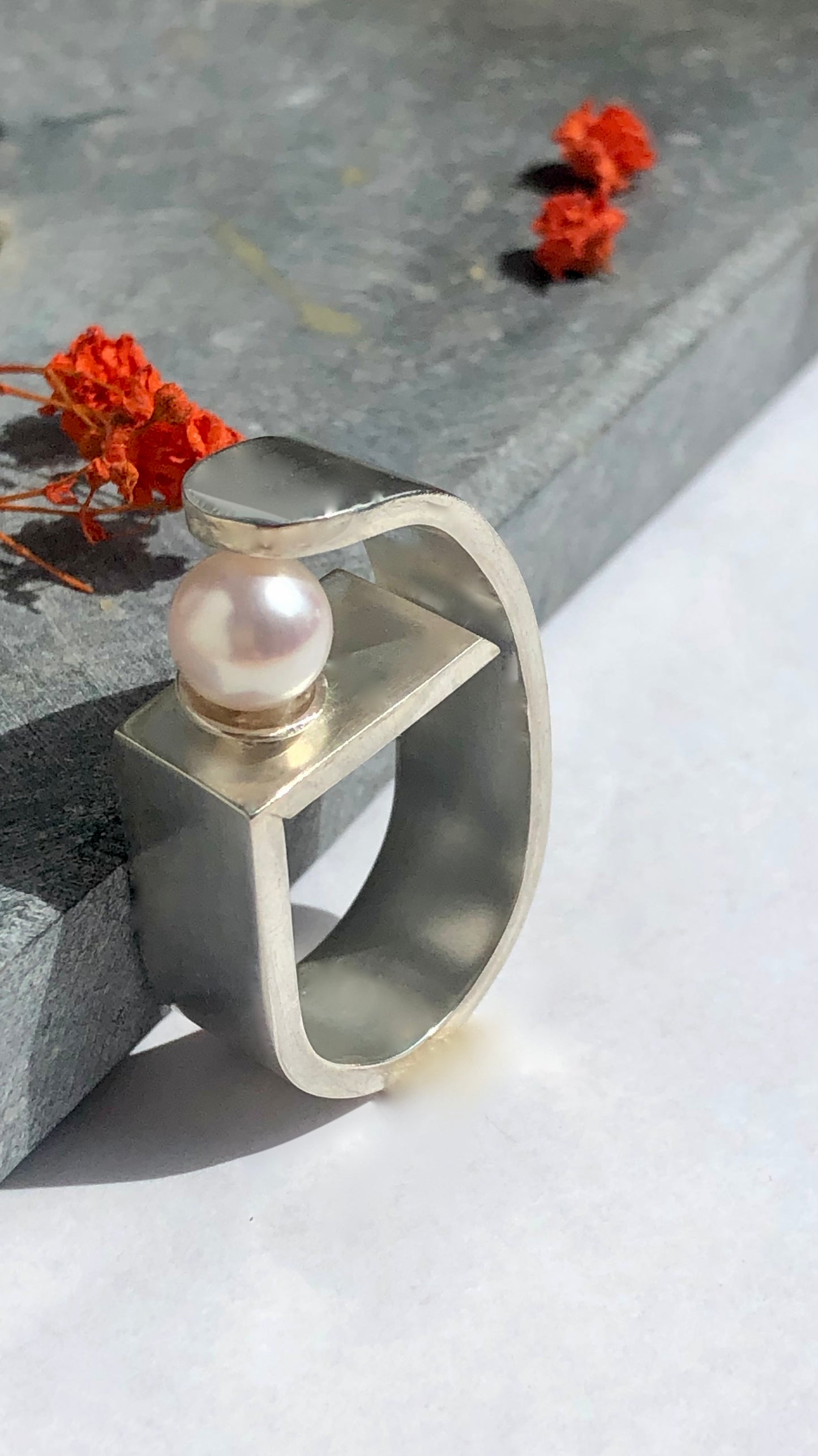 Silver ring with a pearl on a light surface with flowers in the background