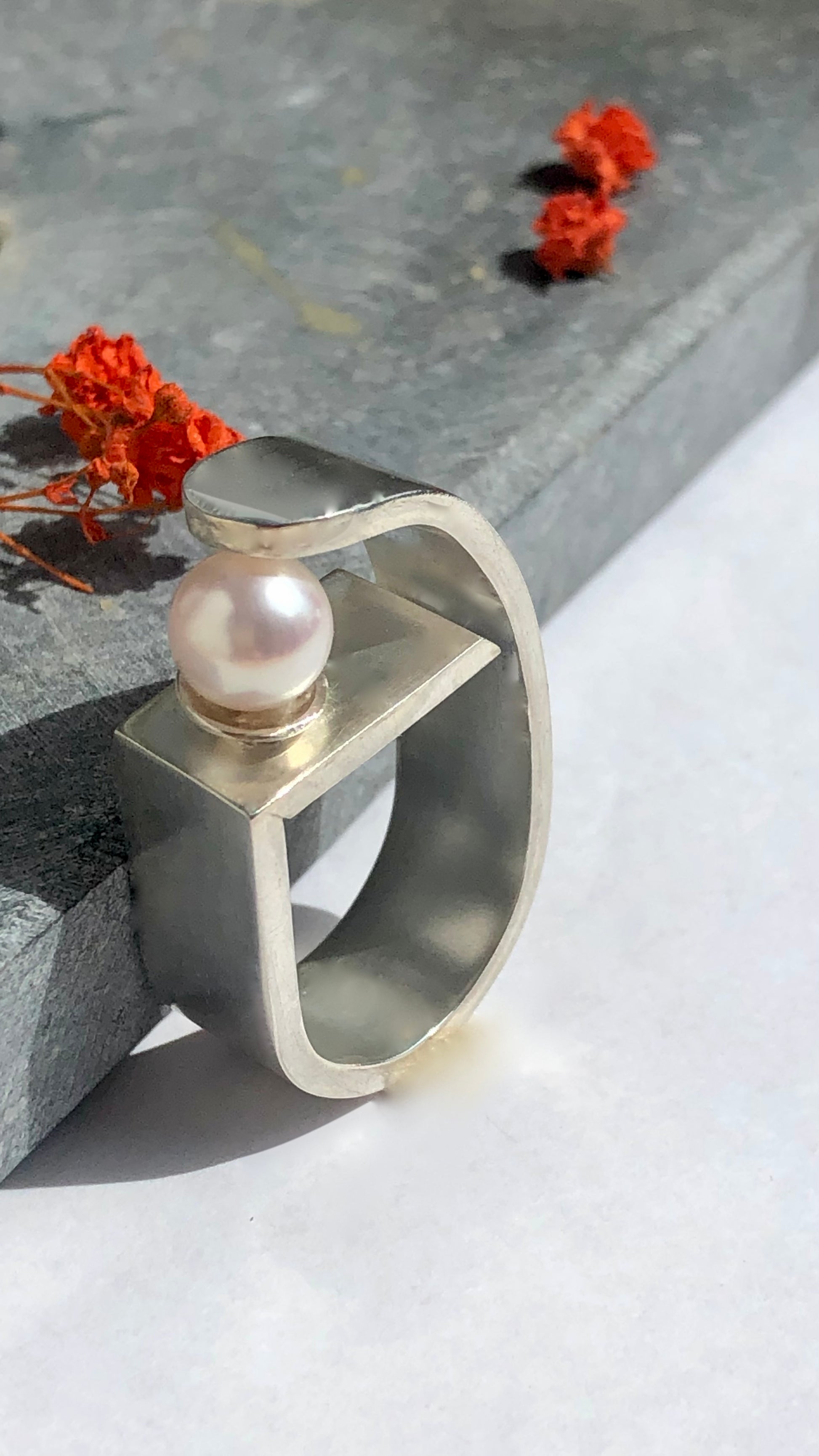 Silver ring with a pearl on a light surface with flowers in the background
