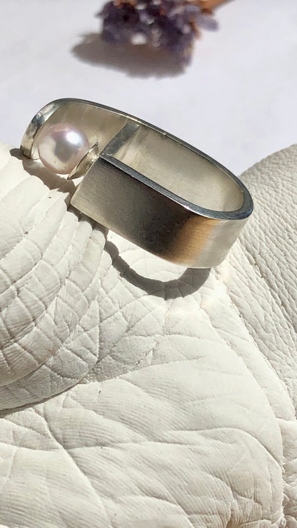 Silver ring with a pearl on a textured surface