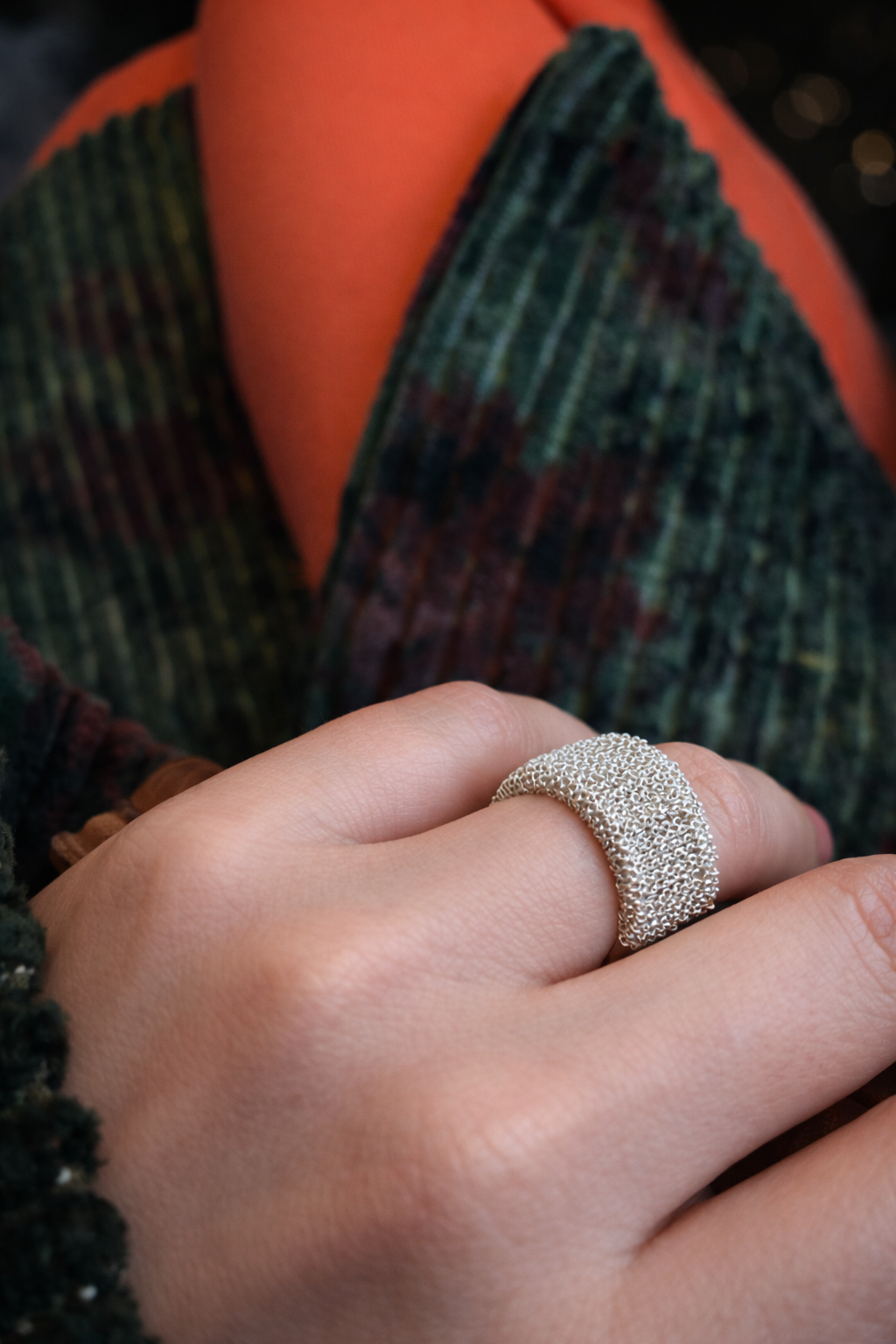 Close-up of a hand wearing a textured silver ring with a blurred background