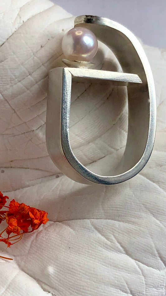 Silver ring with a pearl on a textured white surface