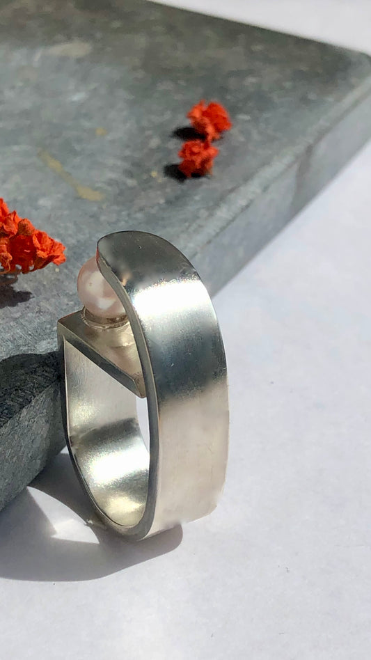 Silver ring with a pearl on a stone surface with red flowers
