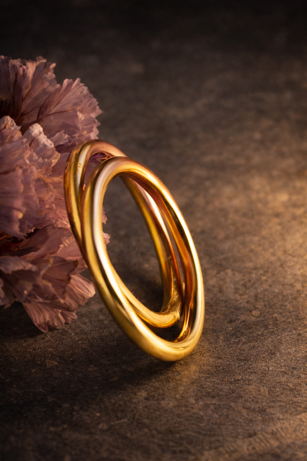 Gold ring on a textured dark surface with a pink flower