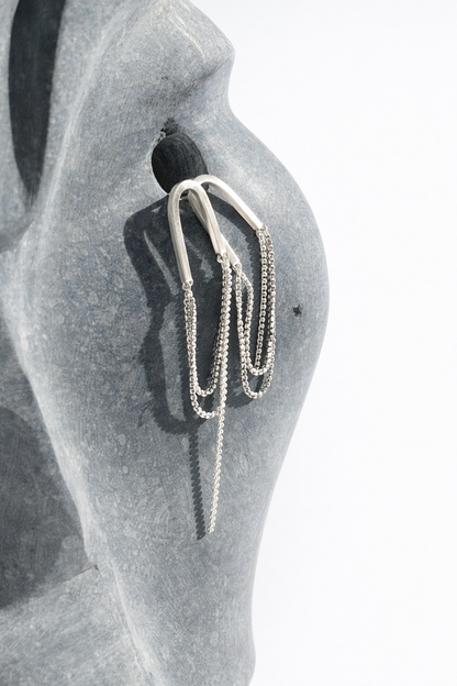 Silver earring on a mannequin ear with a plain background